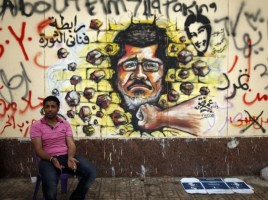 Protester_opposing_President_Mohamed_Morsi_sits_next_to_graffiti_depicting_Morsi_on_a_wall_in_Cairo_1-Jul-2013VOA